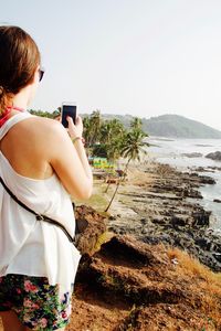 Cropped image of woman photographing beach while standing on hill