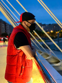 Side view of man standing on railing against sky