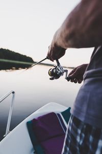 Midsection of man fishing in lake during sunset