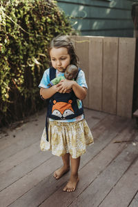 Girl holding woman standing against wood