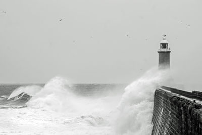 Lighthouse by sea against clear sky