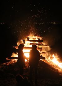 Silhouette people standing by bonfire at night