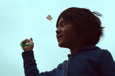 Low angle view of boy with eyes closed flying kite in sky