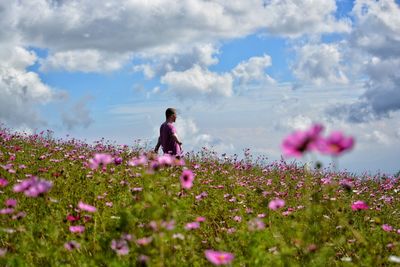 Side view of carefree man standing amidst flowering plants on field against cloudy sky