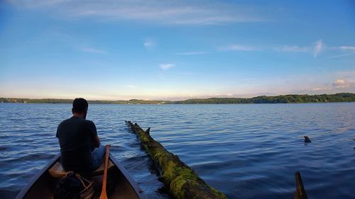 Rear view of man sitting on lake against sky