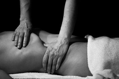 Cropped hands of masseur giving massage to woman against black background