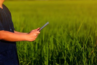 Midsection of farmer using digital tablet on grassy land