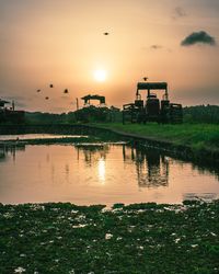 Tractors by lake against sky during sunset