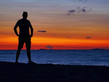 Silhouette man looking at sea against sky during sunset