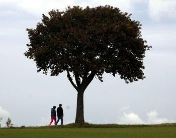 People standing by tree on field against sky