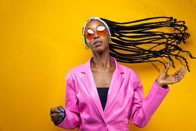 Portrait of young woman standing against yellow background