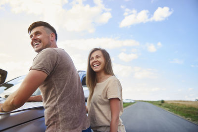Smiling couple standing by car against sky