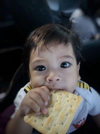 Portrait of cute baby boy eating cracker at home