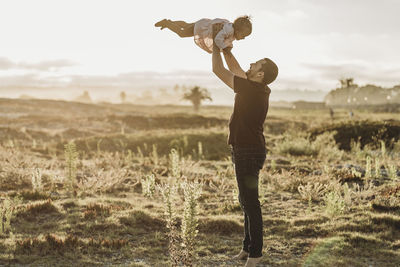 Father playing with young girl at beach during sunset