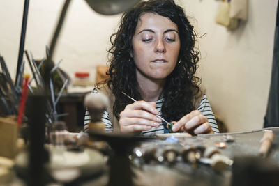 Midsection of female artisan making ring while sitting at table in workshop