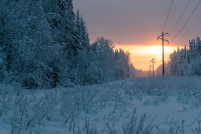 Snow covered field against sky during sunset