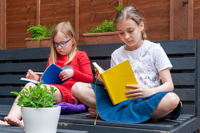 Two school age girls sitting together in garden and doing homework.