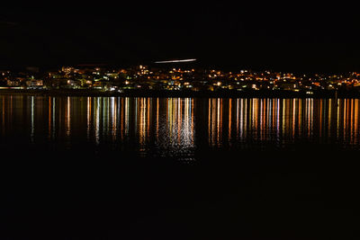 Illuminated buildings by sea against sky at night