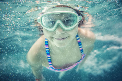 Girl wearing goggles swimming toward camera underwater