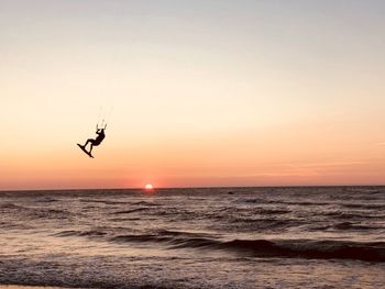 Silhouette person parasailing with surfboard in sea against sky during sunset