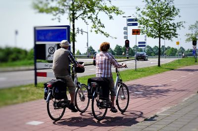 Rear view of people riding bicycle on road