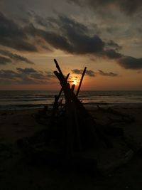 Silhouette driftwood on beach against sky during sunset