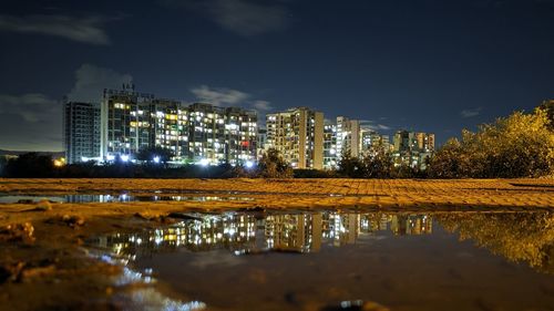 Illuminated buildings by lake against sky in city at night