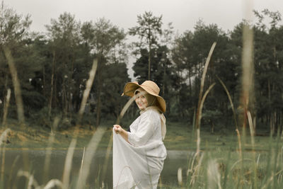 Woman standing by plants against trees