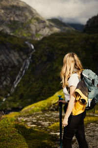 Side view of young woman photographing while standing against mountain