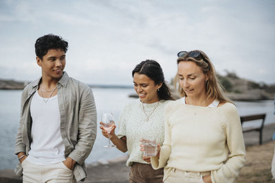 Man talking with female friends holding drinks while walking near lake