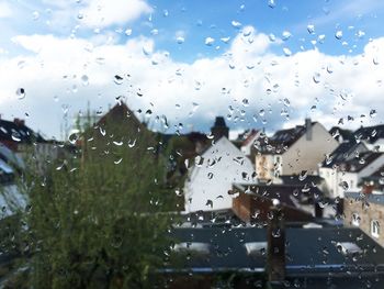 Water drops on glass window against houses