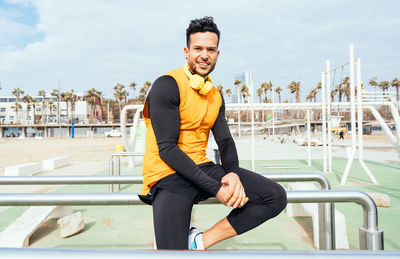 Portrait of smiling man with headphones sitting on railing