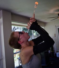 Side view of young woman blowing while standing at home