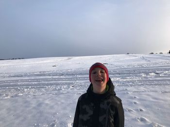 Portrait of smiling boy standing on snow covered landscape against sky during sunset