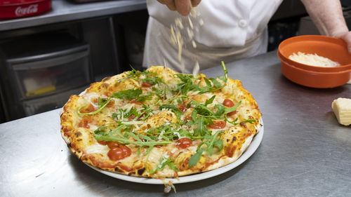 Delicious freshly baked pizza preparation. humand hand put cheese on it.