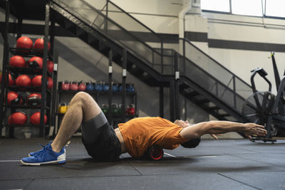 Male athlete with arms raised practicing on pilates rolls in gym