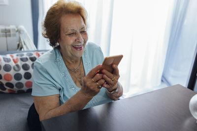 Happy senior woman using smart phone sitting at home