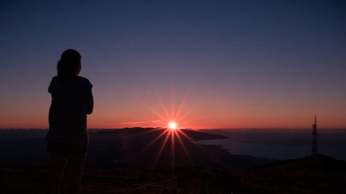 Rear view of silhouette woman standing at beach against clear sky during sunset