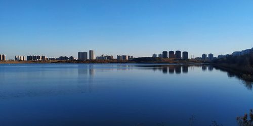 Scenic view of river by buildings against clear blue sky