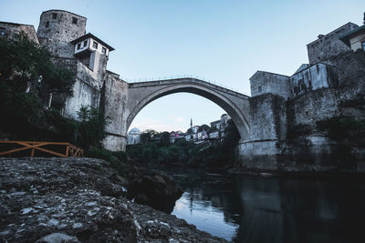 Arch bridge over river amidst buildings against clear sky