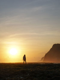 Silhouette woman standing at beach against sky during sunset