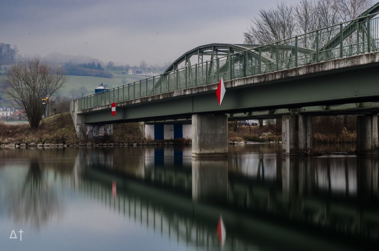 architecture, connection, water, built structure, bridge - man made structure, river, waterfront, building exterior, reflection, sky, engineering, day, outdoors, bridge, no people, riverbank, tranquility