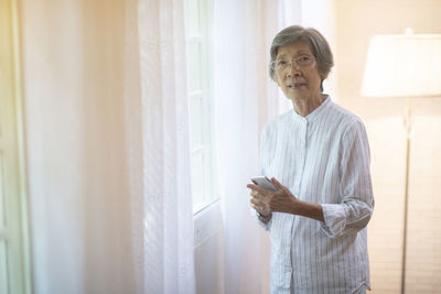 Portrait of senior woman holding smart phone standing at home