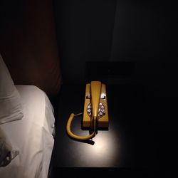 High angle view of old-fashioned yellow telephone by bed on table