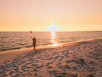 Woman playing with plastic disc at beach against sky during sunset