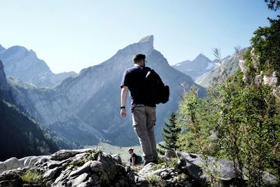 Rear view of man standing on rock against mountains