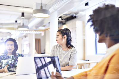 Businesswomen looking at female colleague explaining while sitting at conference table