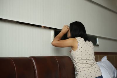 Side view of woman standing by wall at home