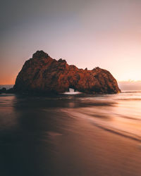 Rock formations in sea against clear sky during sunset