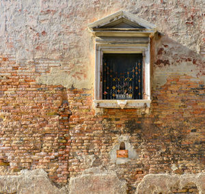 White window on old house wall cracks in concrete visible red bricks in venice, italy.